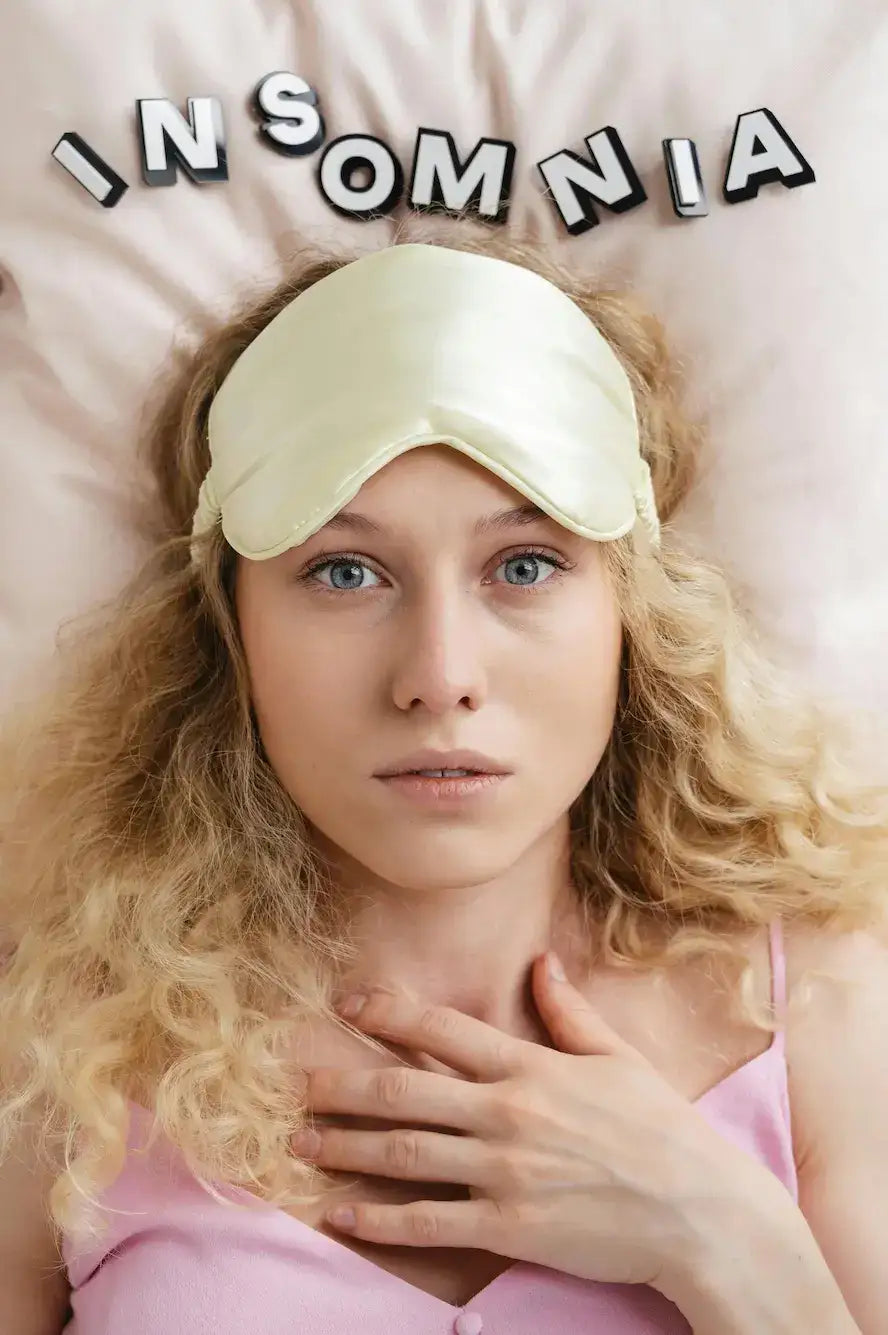 Woman with a sleep mask and blonde hair lying on a pillow with 'INSOMNIA' spelled in letters.