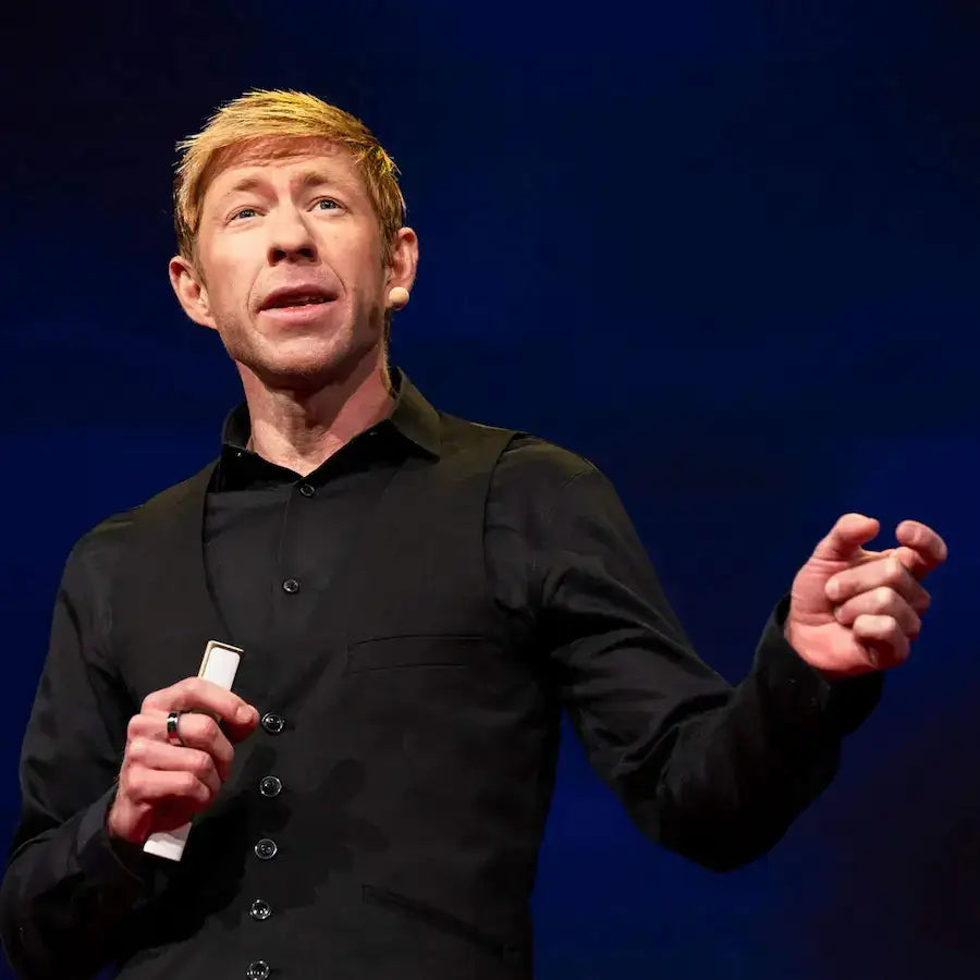 A blonde man in a black shirt giving a presentation against a dark blue background.