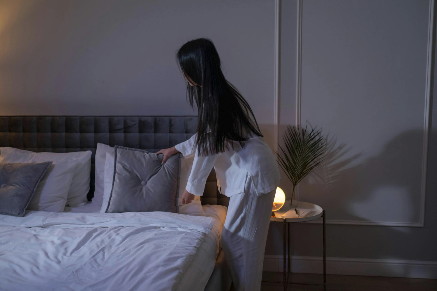 Woman moving cushions on bed getting ready to get into bed.
